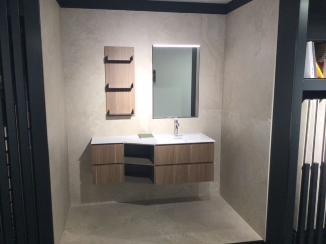 Mobile bagno moderno con specchio, lavabo e ante in legno in una stanza minimalista sui toni del grigio.