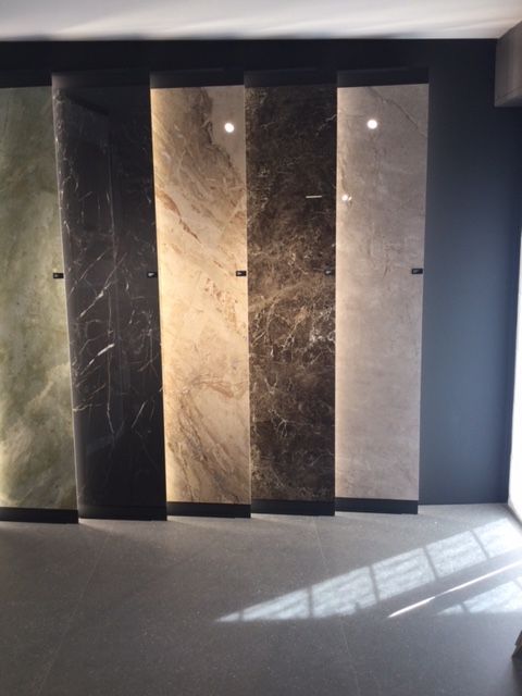 Showroom moderno con quattro alti pannelli in marmo/pietra nei toni scuri e chiari, luce solare sul pavimento