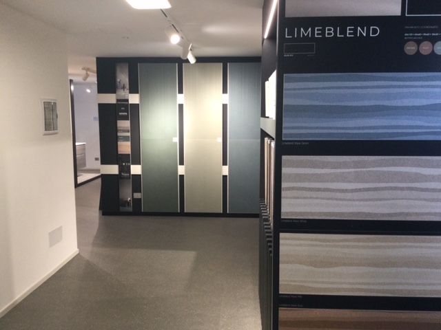 Showroom moderno con pannelli in vetro satinato e un'esposizione LIMEBLEND di campioni con diverse texture.