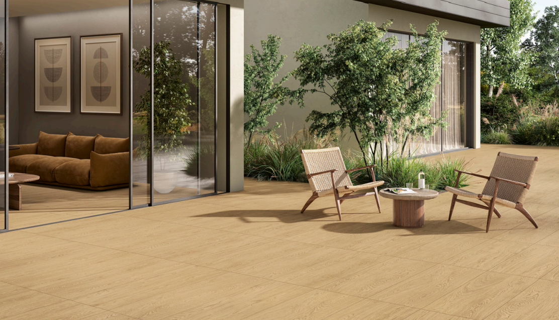 Patio moderno con sedie a sdraio, tavolino, albero in vaso e grandi porte scorrevoli in vetro accanto a una casa.