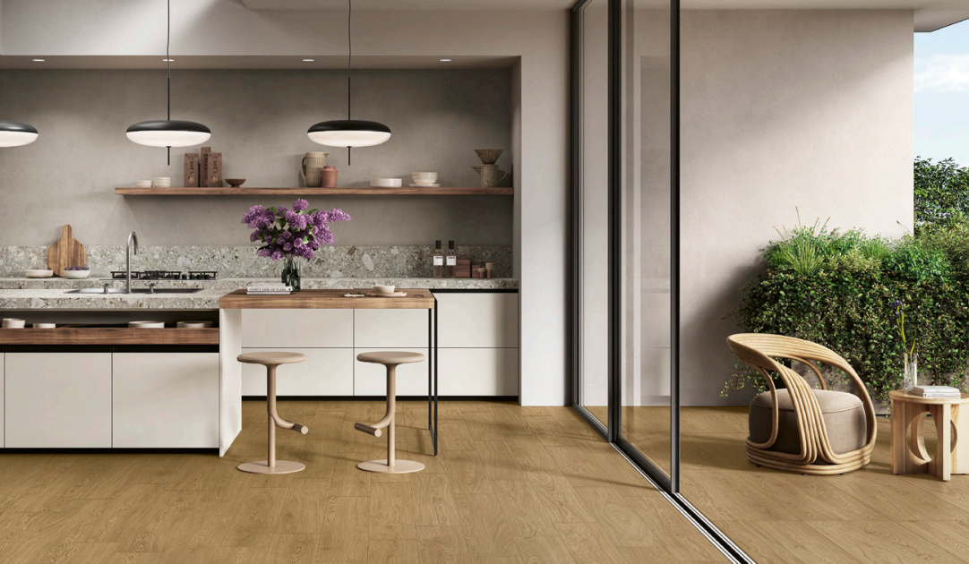 Cucina moderna con accesso al patio tramite porte scorrevoli in vetro, pavimento in legno, tavolo a isola, fiori e sedia in rattan.