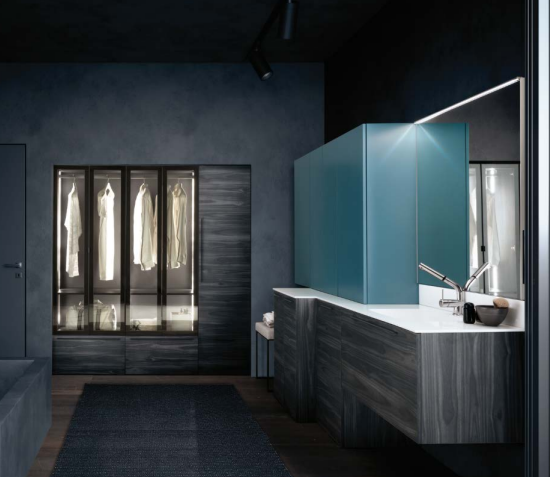 Bagno moderno con pareti scure, mobile lavabo blu, specchio e armadio illuminato sullo sfondo.