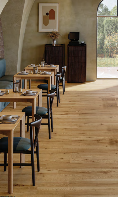 Sala da pranzo moderna con tavoli in legno, sedie color verde acqua e una finestra soleggiata che si affaccia sul verde.