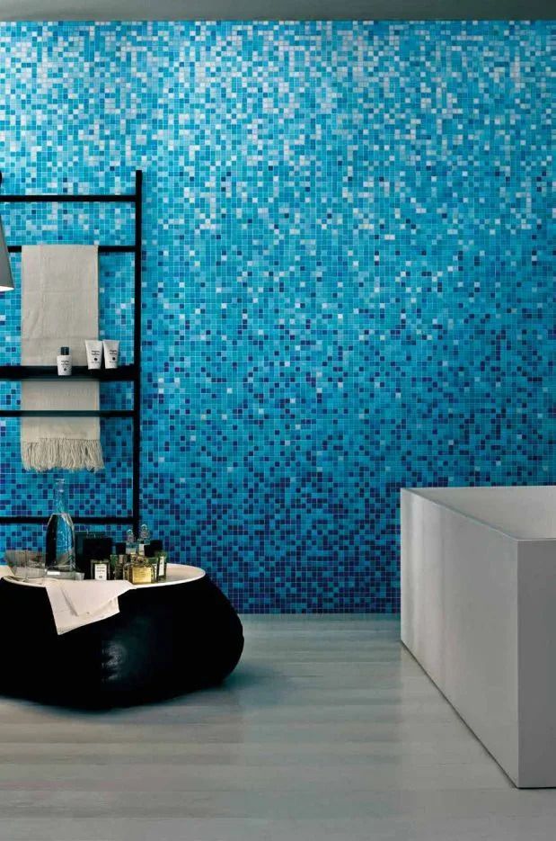 Spa moderna con parete a mosaico blu, sedia nera, portasciugamani e panca bianca.