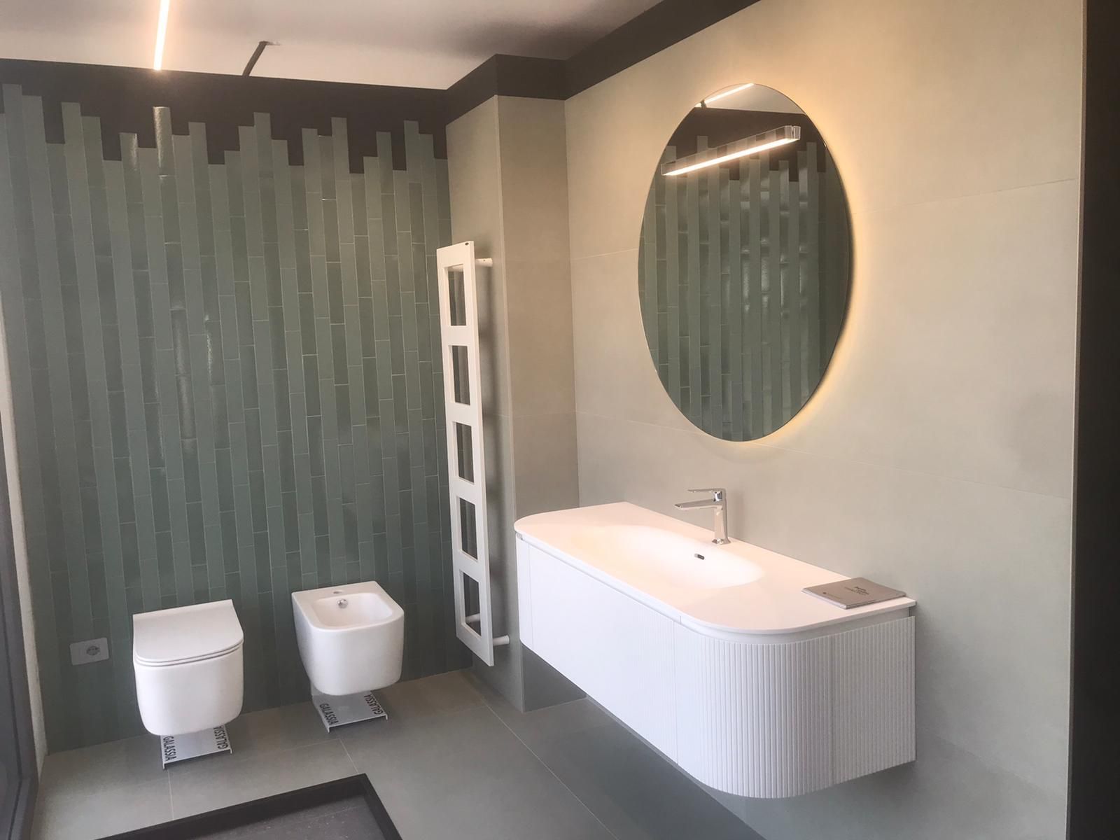 Bagno moderno con pareti grigie, lavabo a parete, specchio ovale e WC e bidet accanto alla zona doccia.