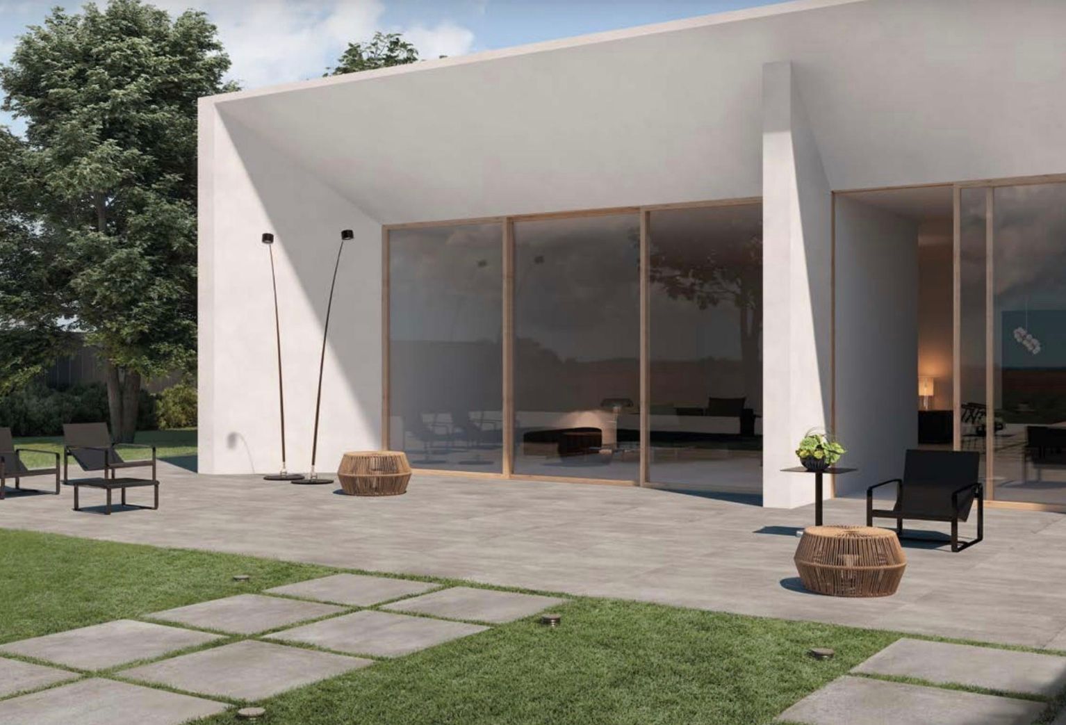 Patio moderno di una casa bianca con porte scorrevoli in vetro, sedie nere e prato con pavimentazione in pietra.