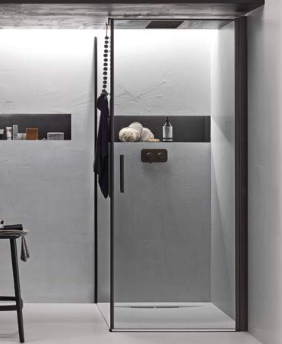 Bagno moderno con box doccia in vetro e pareti piastrellate di grigio, dotato di mensola con articoli da toeletta.