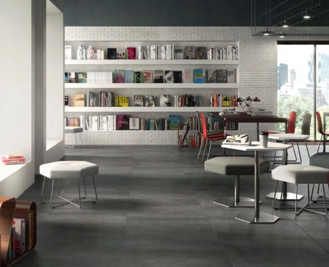 Interno moderno di una caffetteria con scaffali bianchi pieni di libri, tavoli, sedie e ampie vetrate.