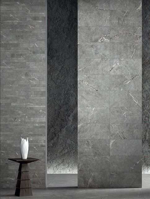 Interno moderno e minimalista con pareti in pietra grigia, una stretta apertura scura e un tavolino con un vaso bianco.