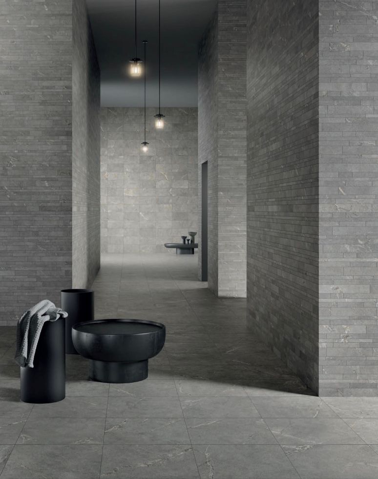 Bagno moderno di colore grigio con lavabo e asciugamano neri in primo piano, lungo corridoio e panca in lontananza.
