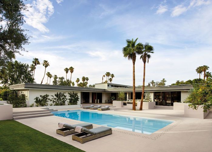 Casa moderna con piscina turchese, lettini prendisole e alte palme sotto un cielo azzurro.