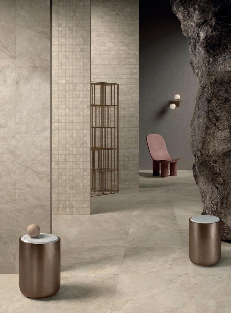 Interno moderno e minimalista con pareti in pietra beige, sedia rosa e tavolini marroni.