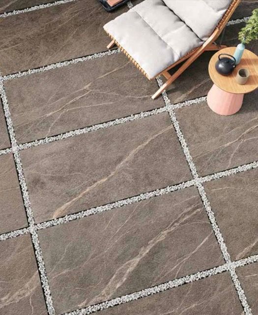 Patio piastrellato di marrone con una poltrona imbottita e un tavolino con lampada.