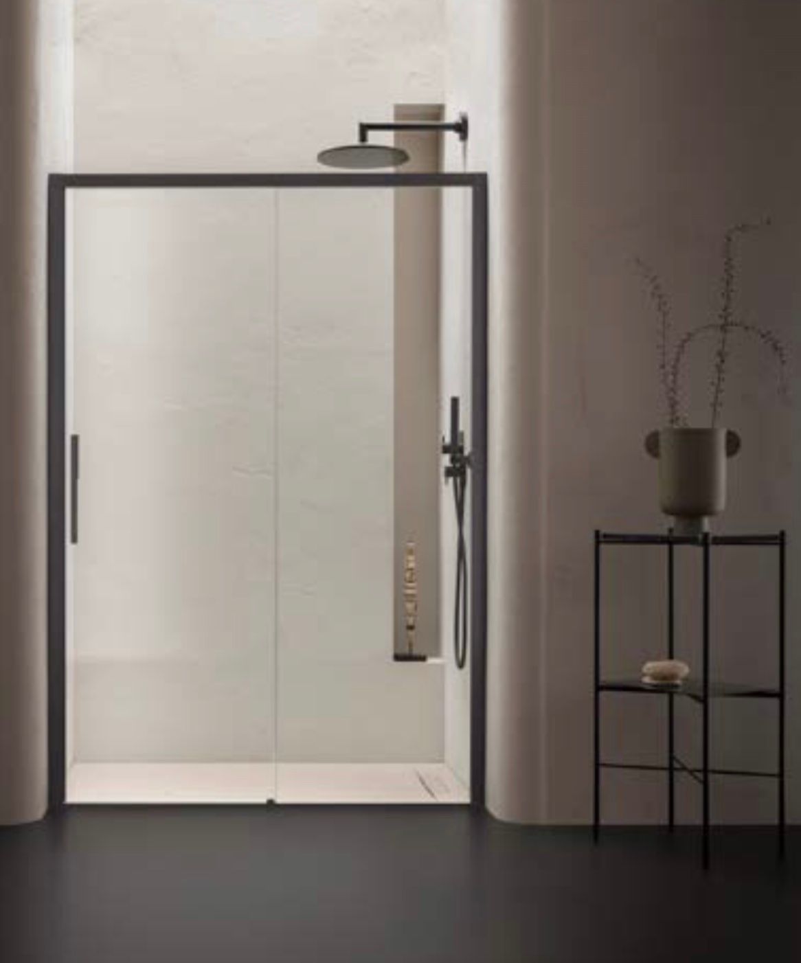 Bagno minimalista con porta doccia in vetro satinato, pavimento scuro e tavolino nero con vaso.