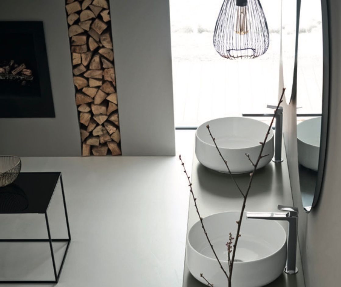 Interno moderno e minimalista con sedie rotonde bianche, un tavolo in vetro, una parete attrezzata in legno e una lampada a sospensione.