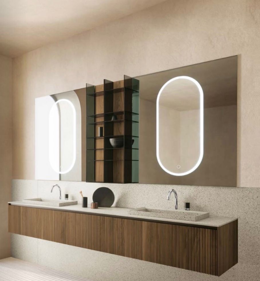 Mobile bagno moderno con due specchi illuminati, mobiletto in legno e piano in pietra beige.