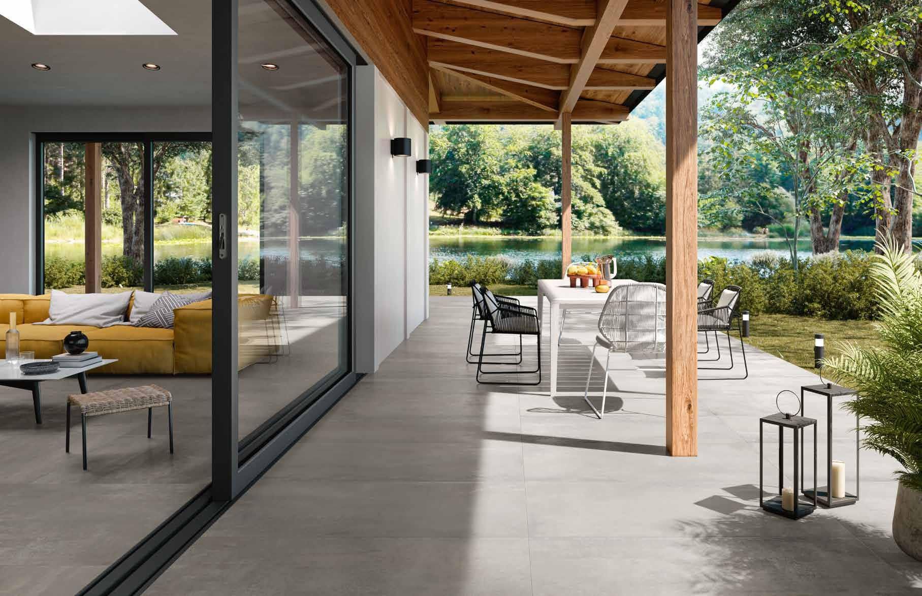 Patio moderno con vista sul giardino, dotato di porte a vetri, travi in ​​legno e posti a sedere all'aperto su una terrazza in cemento.