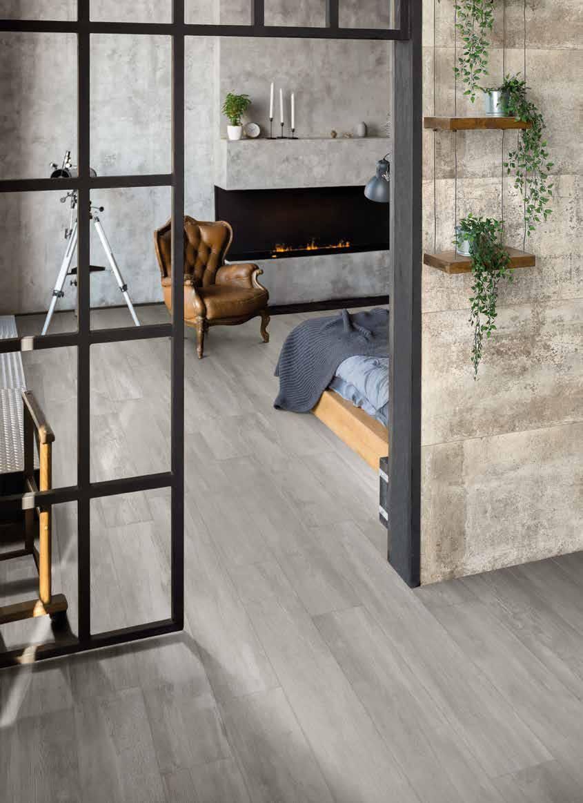 Camera da letto moderna con pavimento grigio, divisorio con cornice nera, camino, poltrona e letto accanto a una parete con finitura materica.