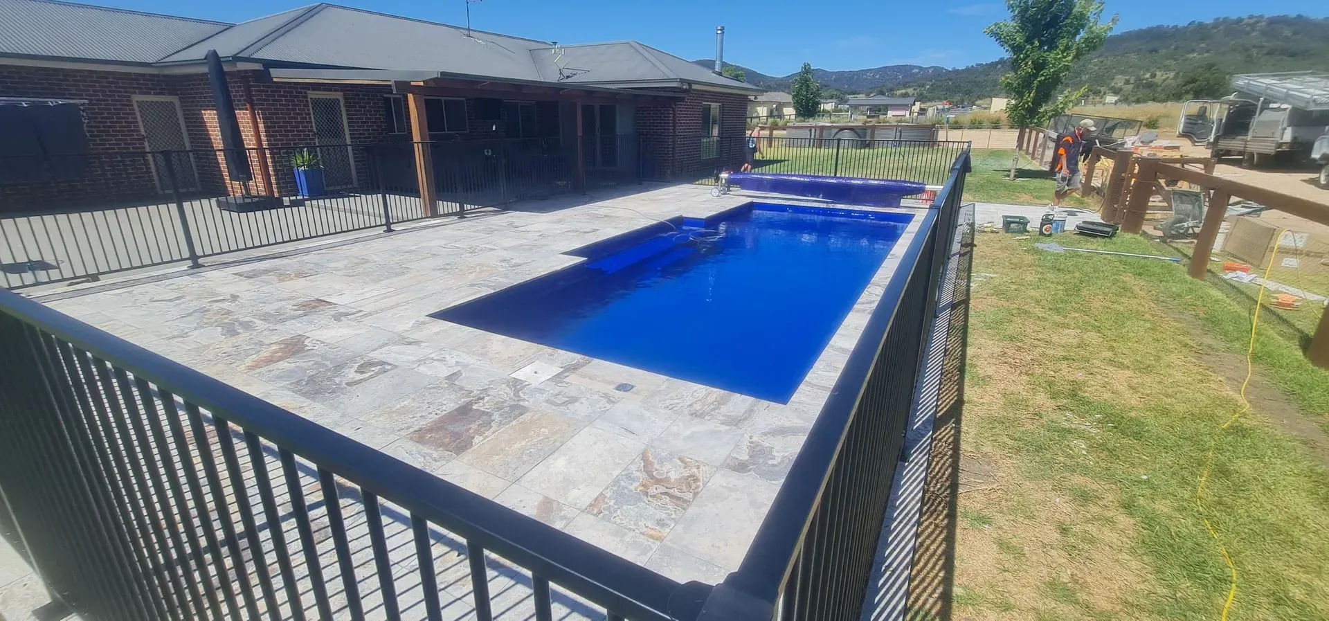A Backyard Swimming Pool Surrounded by a Black Fence and a House — Newcorp Pools In Armidale, NSW