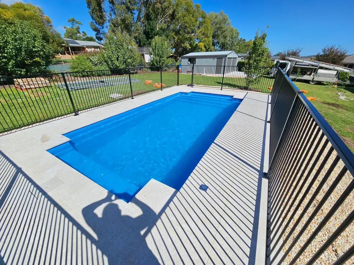 Rectangular Blue Swimming Pool With Concrete Surround and Black Metal Fence in a Yard — Newcorp Pools In Armidale, NSW