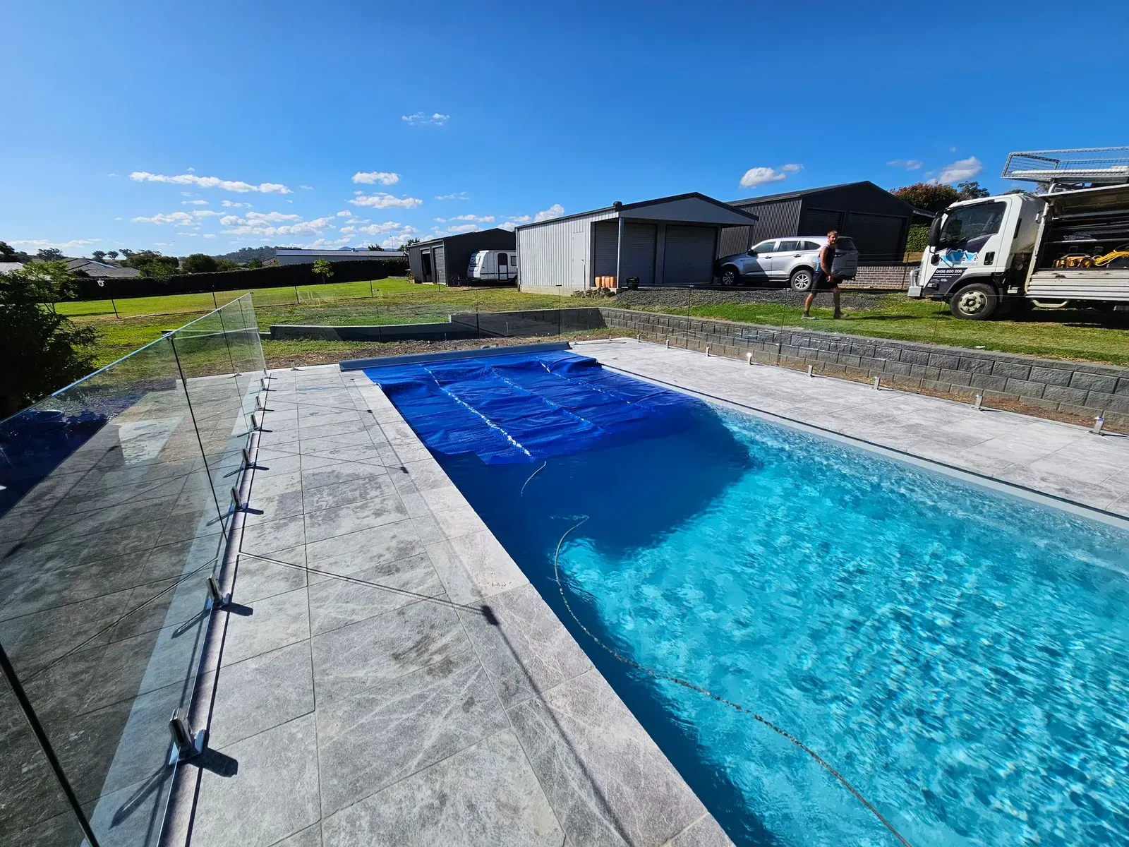 Rectangular Swimming Pool With Blue Water and Cover, Glass Fence, and Buildings — Newcorp Pools In Narrabri, NSW