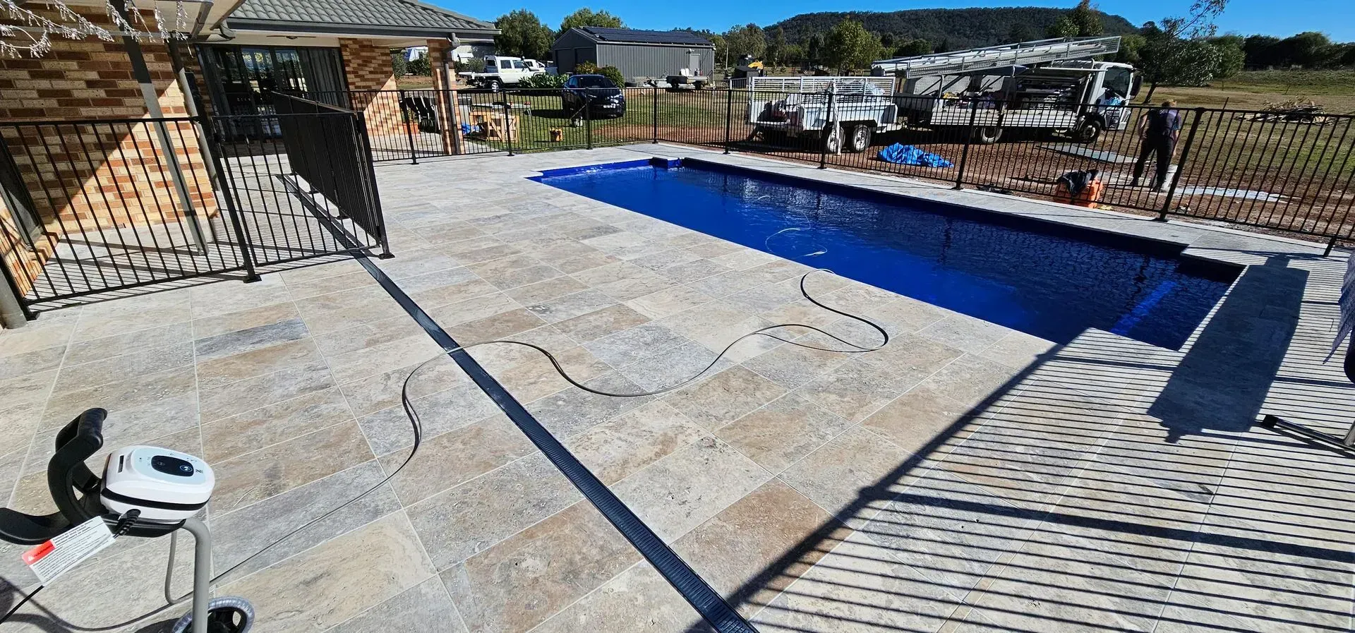A Rectangular Swimming Pool Surrounded by Stone Patio With a Black Metal Fence and House — Newcorp Pools In Narrabri, NSW