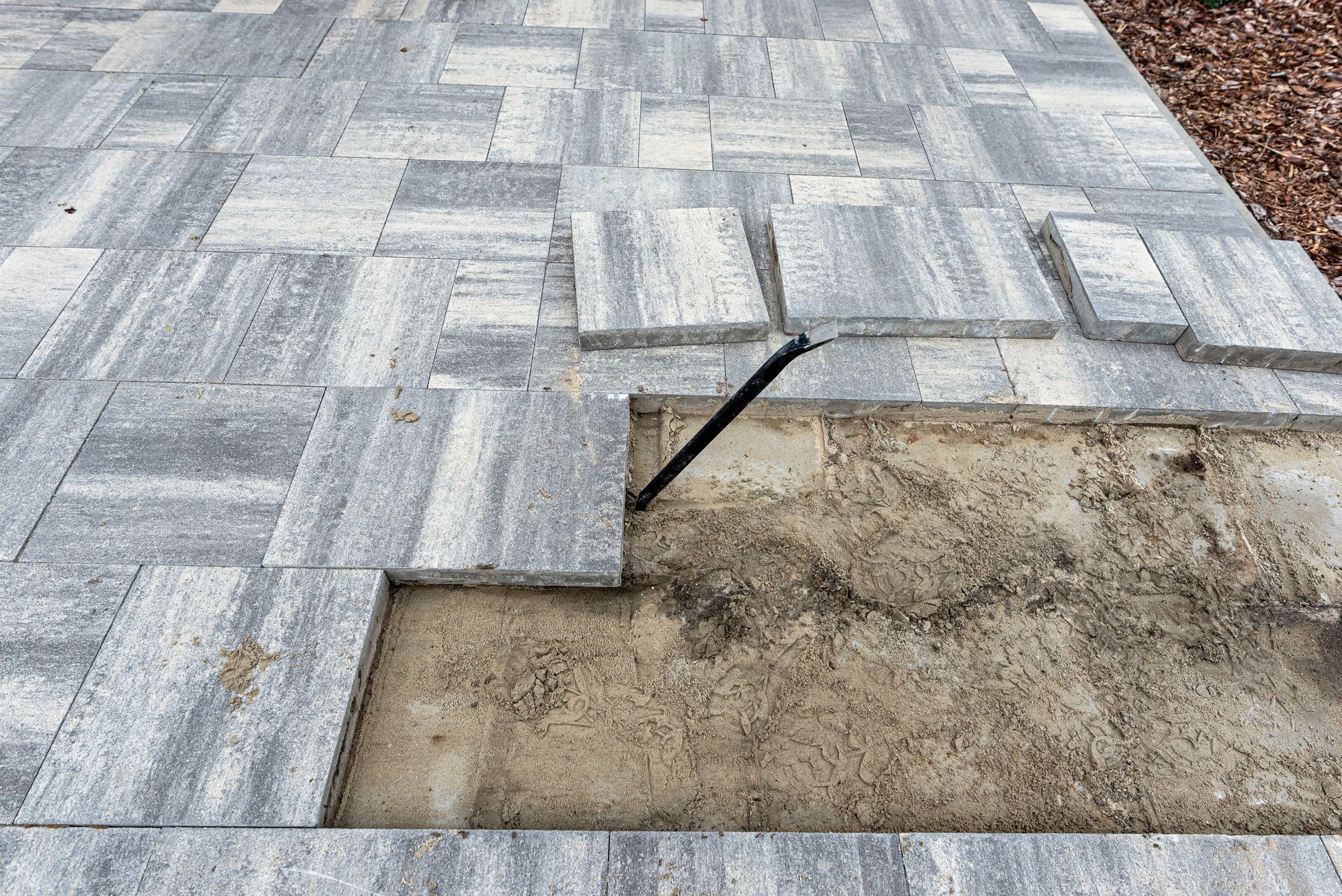 Partially installed gray brick paver walkway with an exposed dirt patch and lifted edging strip