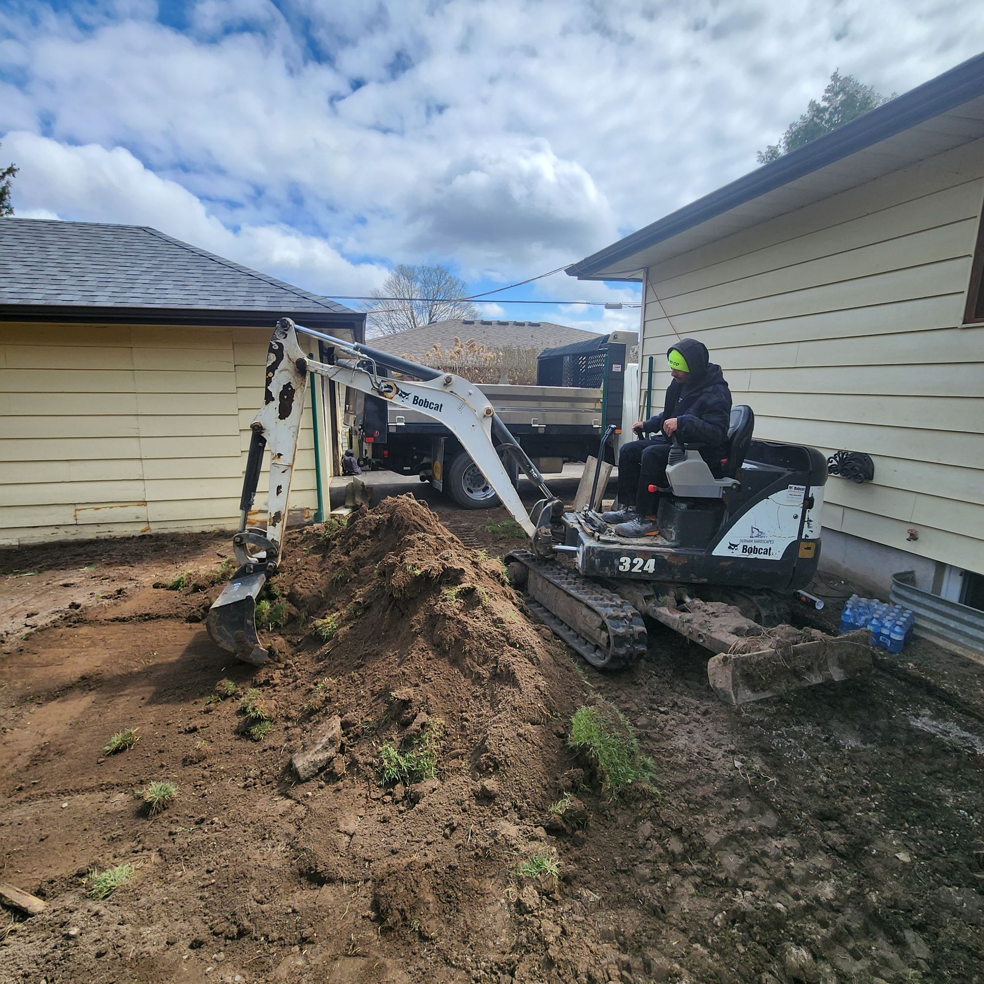 A man is driving a small excavator in front of a house.
