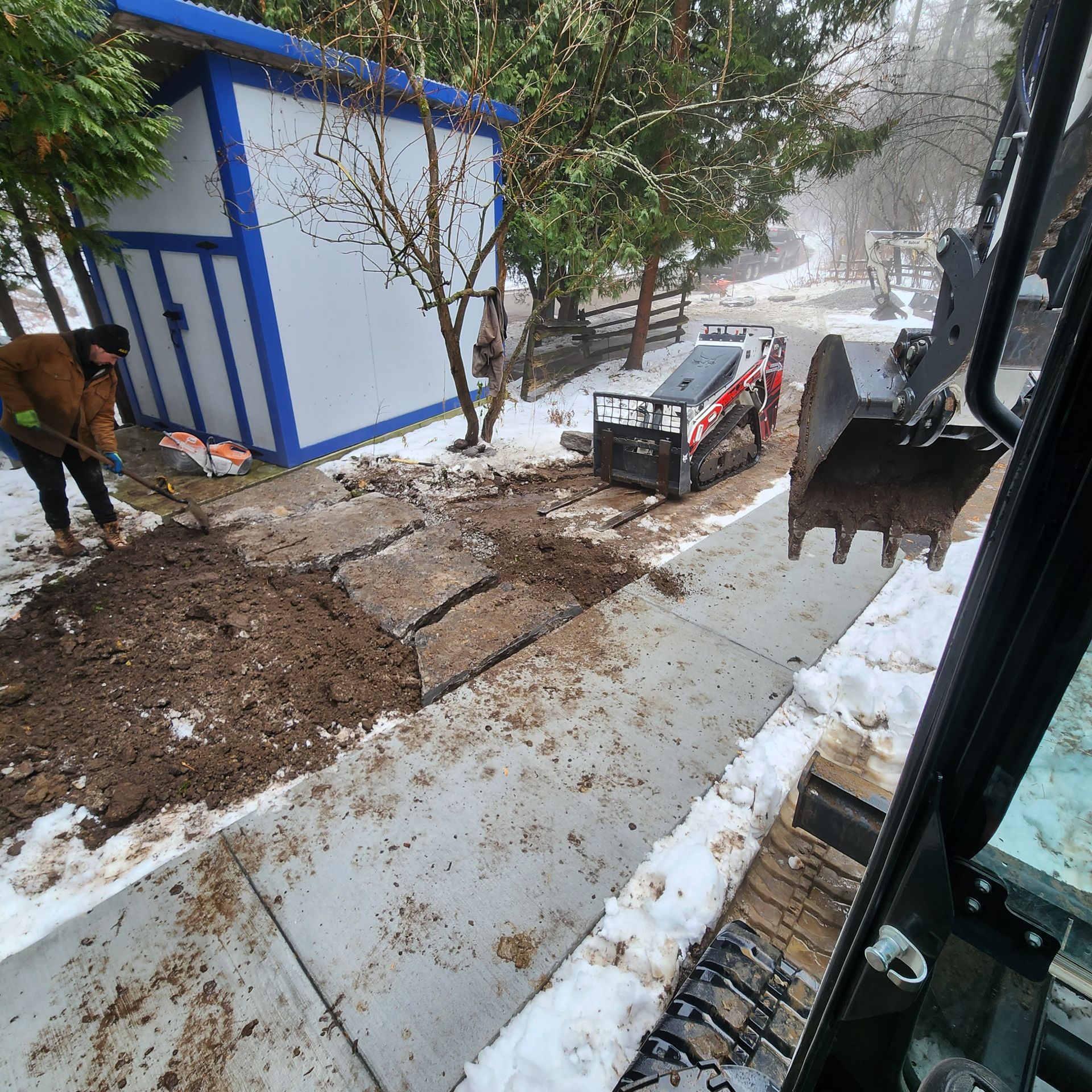 A man is digging in the snow next to a bulldozer.