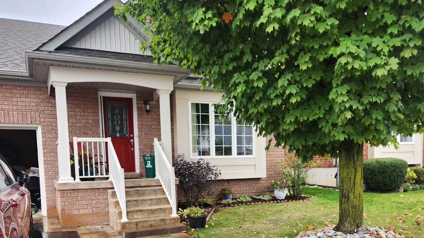 A brick house with a porch and a tree in front of it.