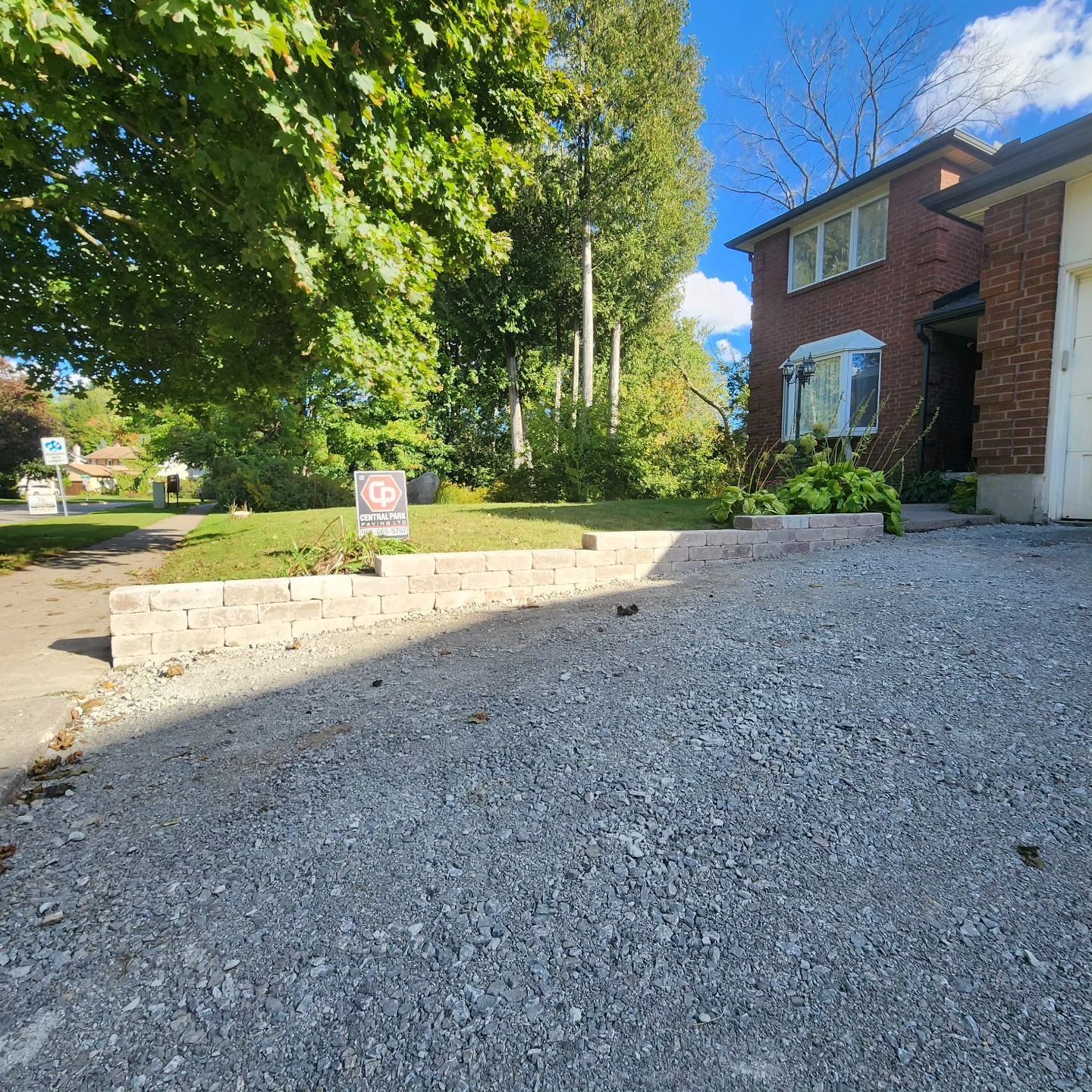 A brick house with a gravel driveway and a for sale sign in front of it.