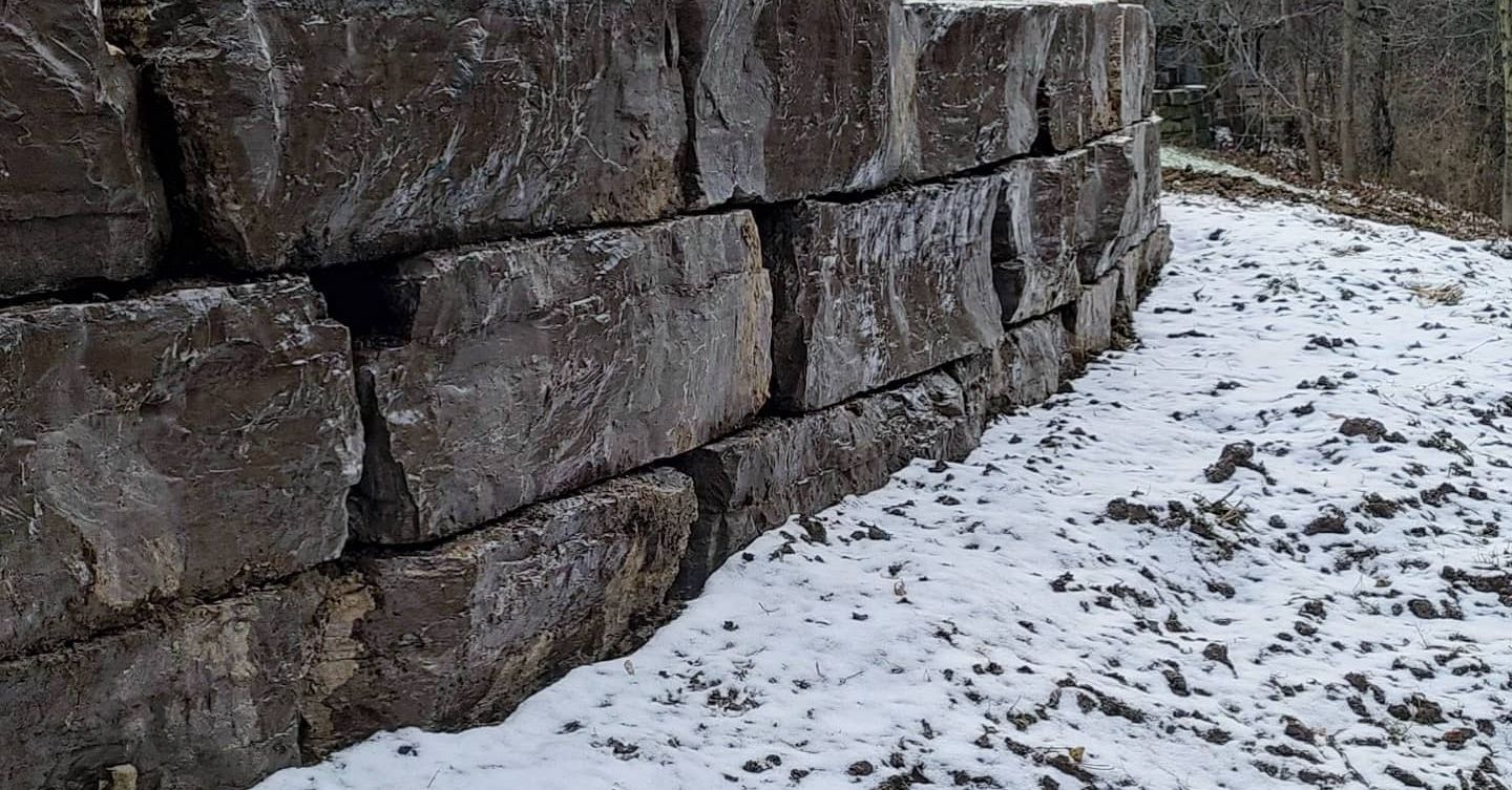 A stone wall with snow on the ground in front of it.