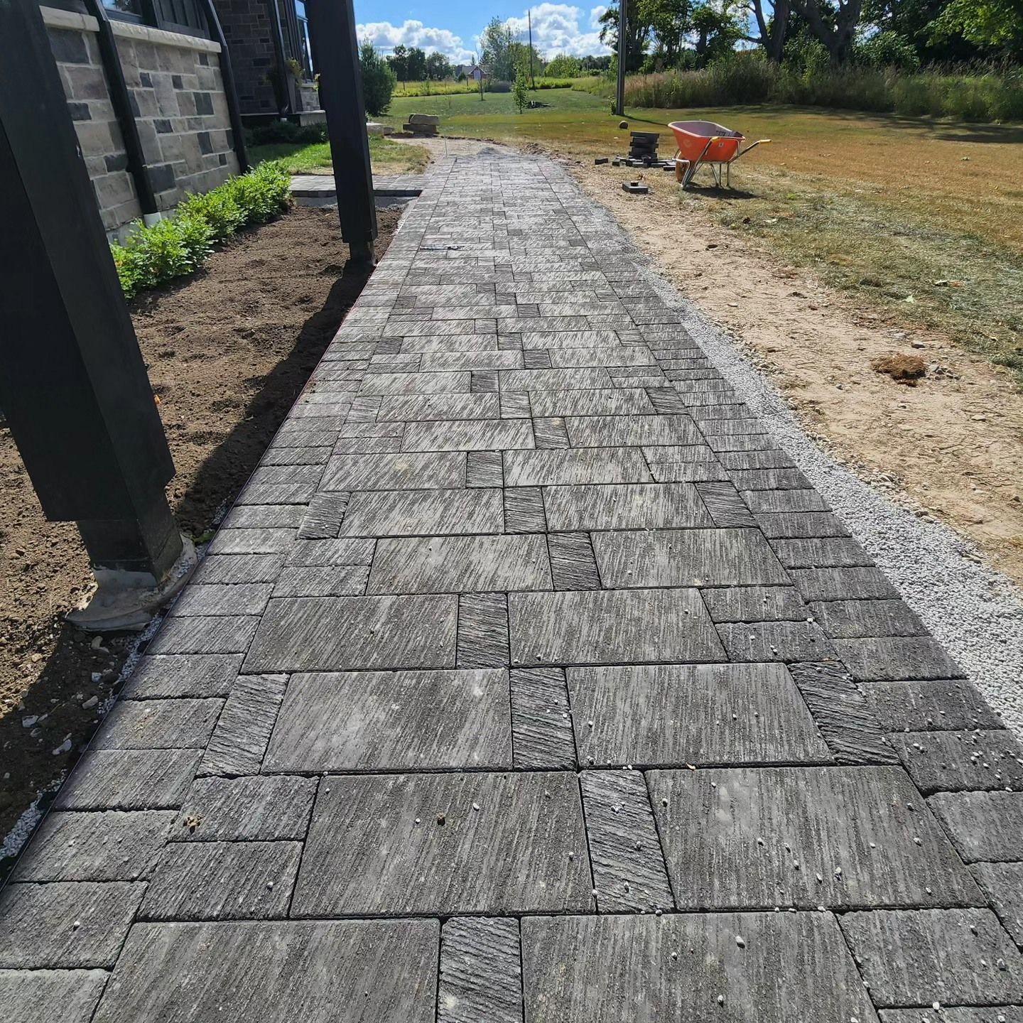 A brick walkway with a wheelbarrow on the side of it.