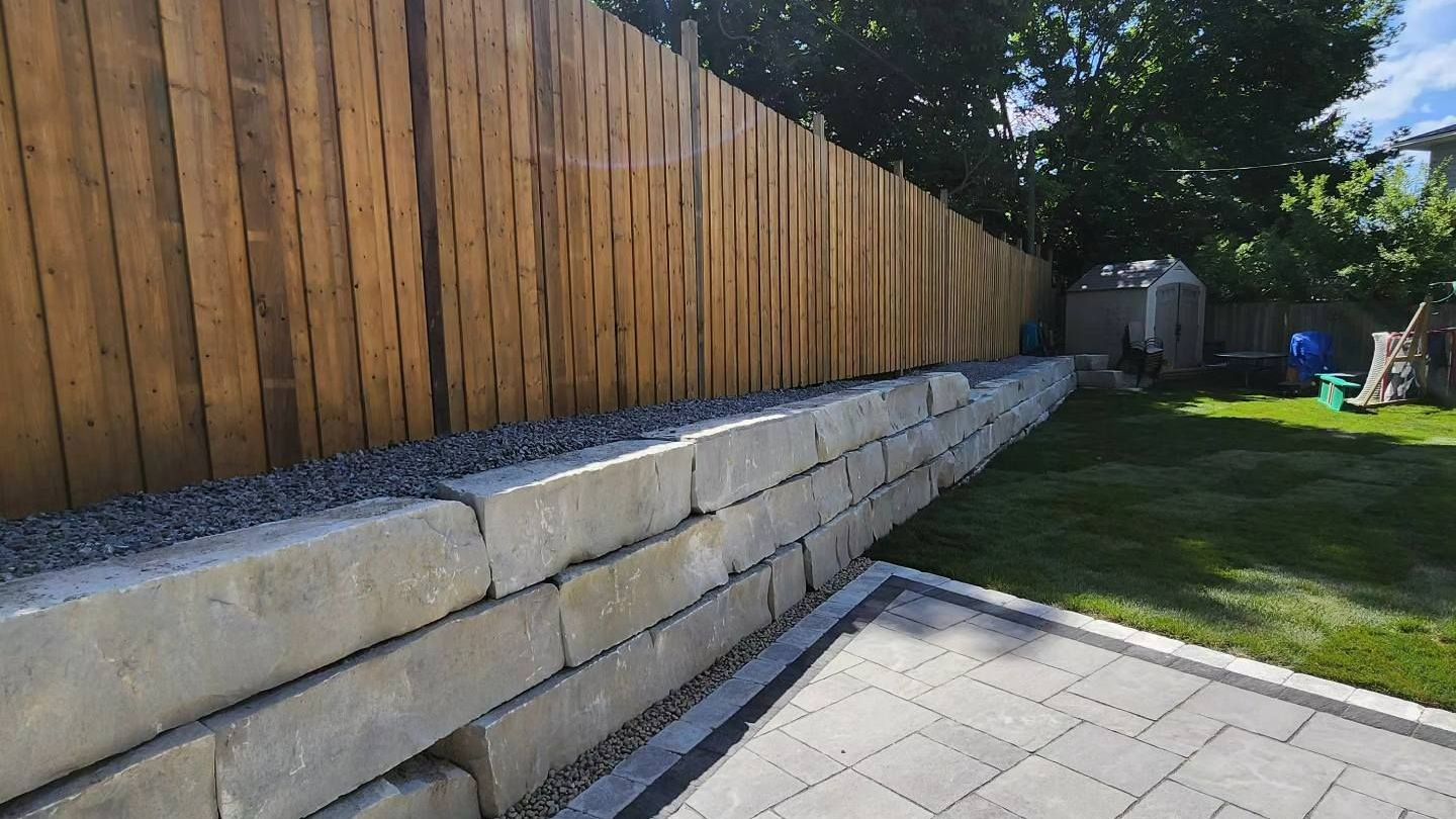 A wooden fence surrounds a brick wall in a backyard.