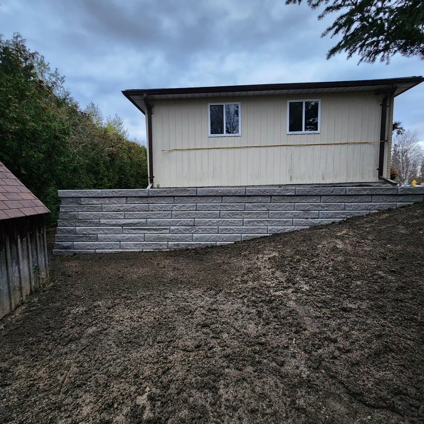 A house is sitting on top of a dirt hill next to a stone wall.