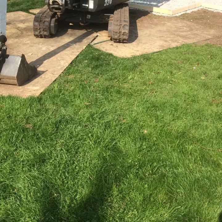 A small excavator is sitting on top of a concrete driveway in a yard.
