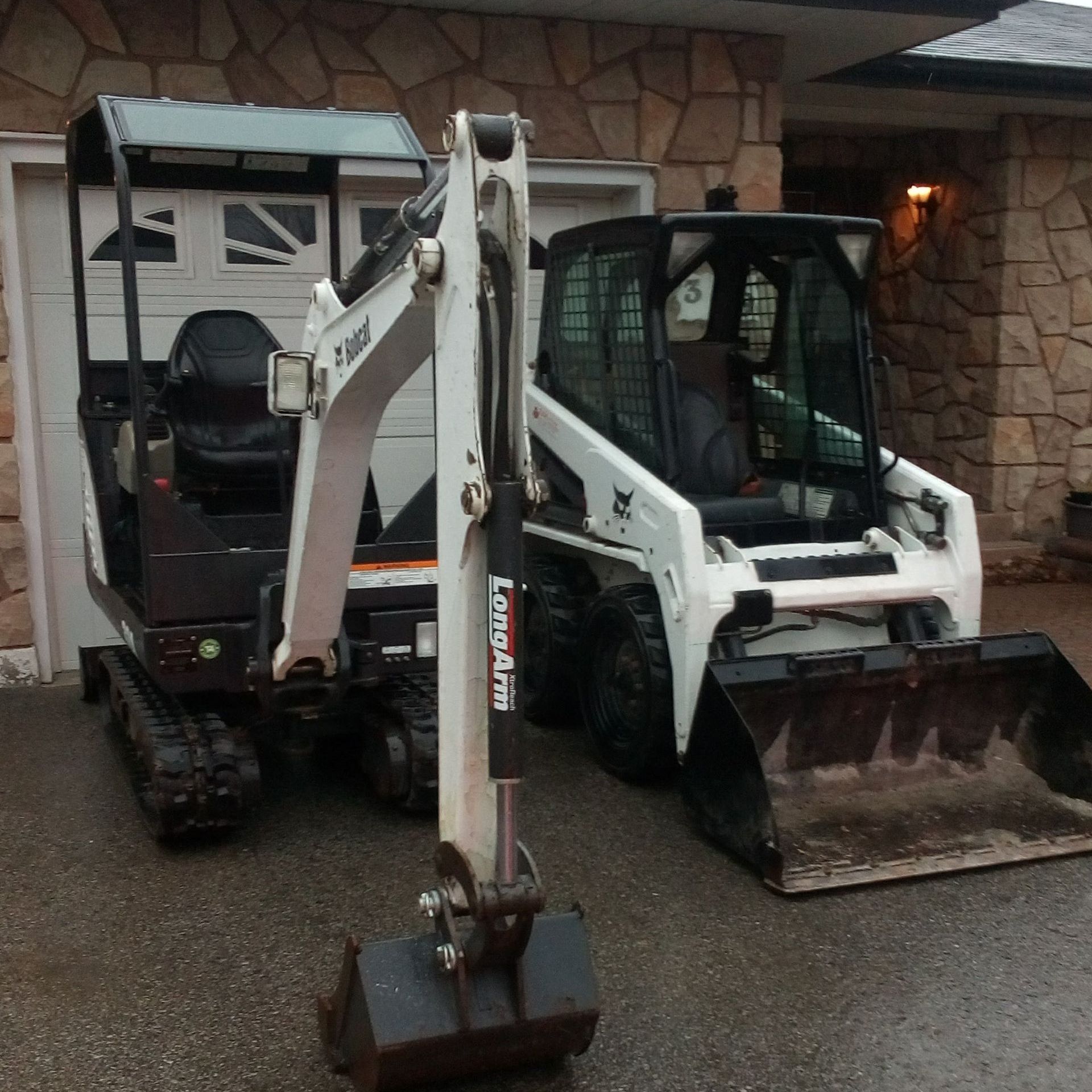 Two bobcat tractors are parked in front of a house.