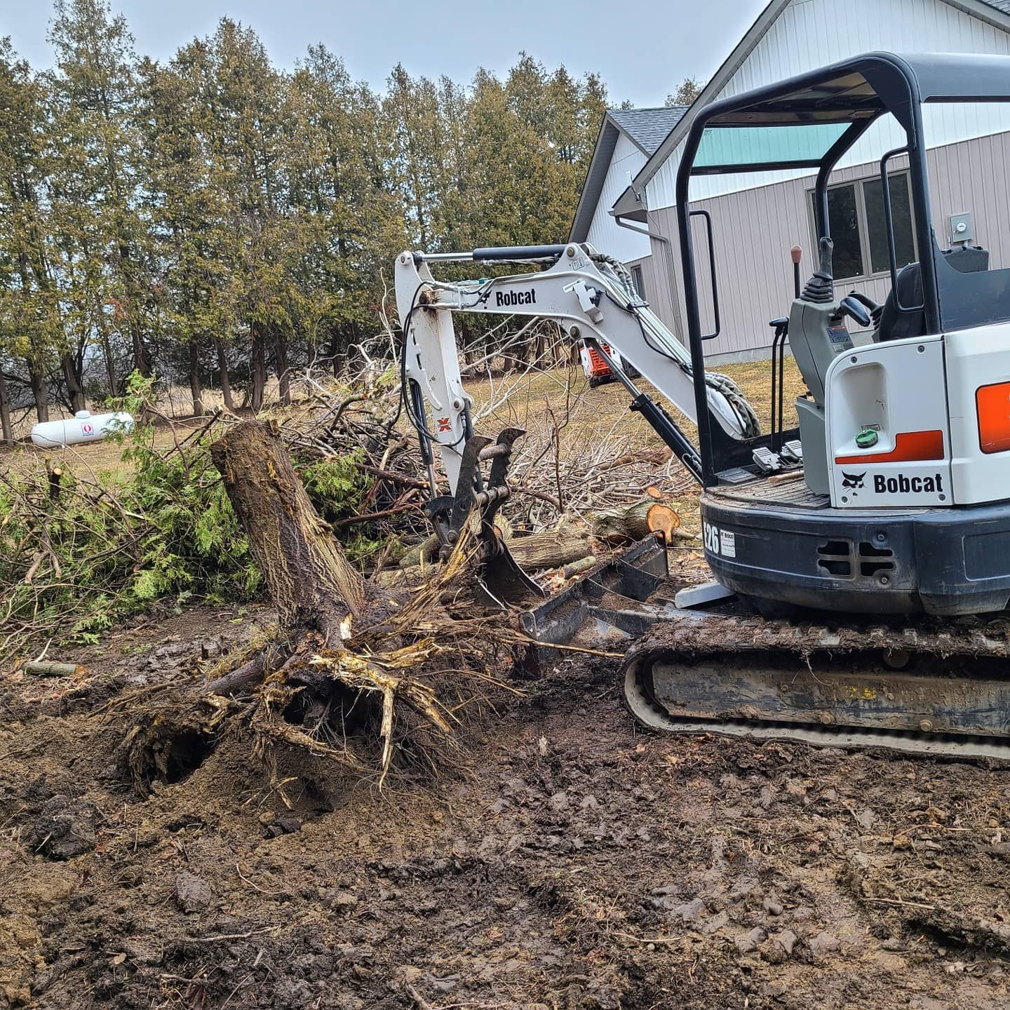 A bobcat excavator is digging a hole in the ground in front of a house.