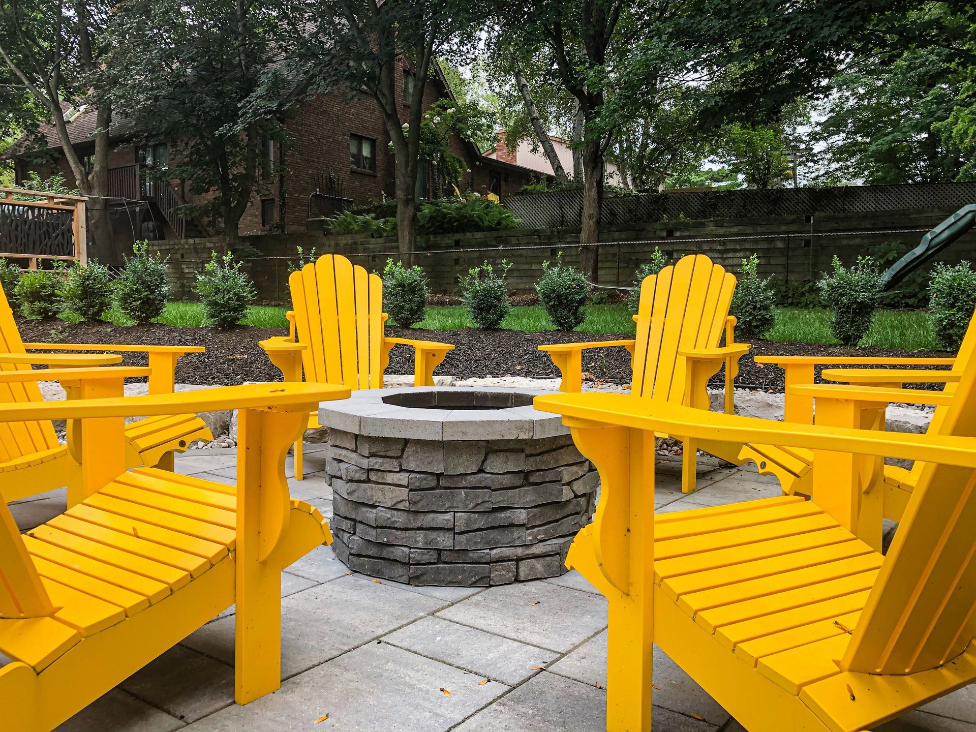 A group of yellow chairs are sitting around a fire pit on a patio.