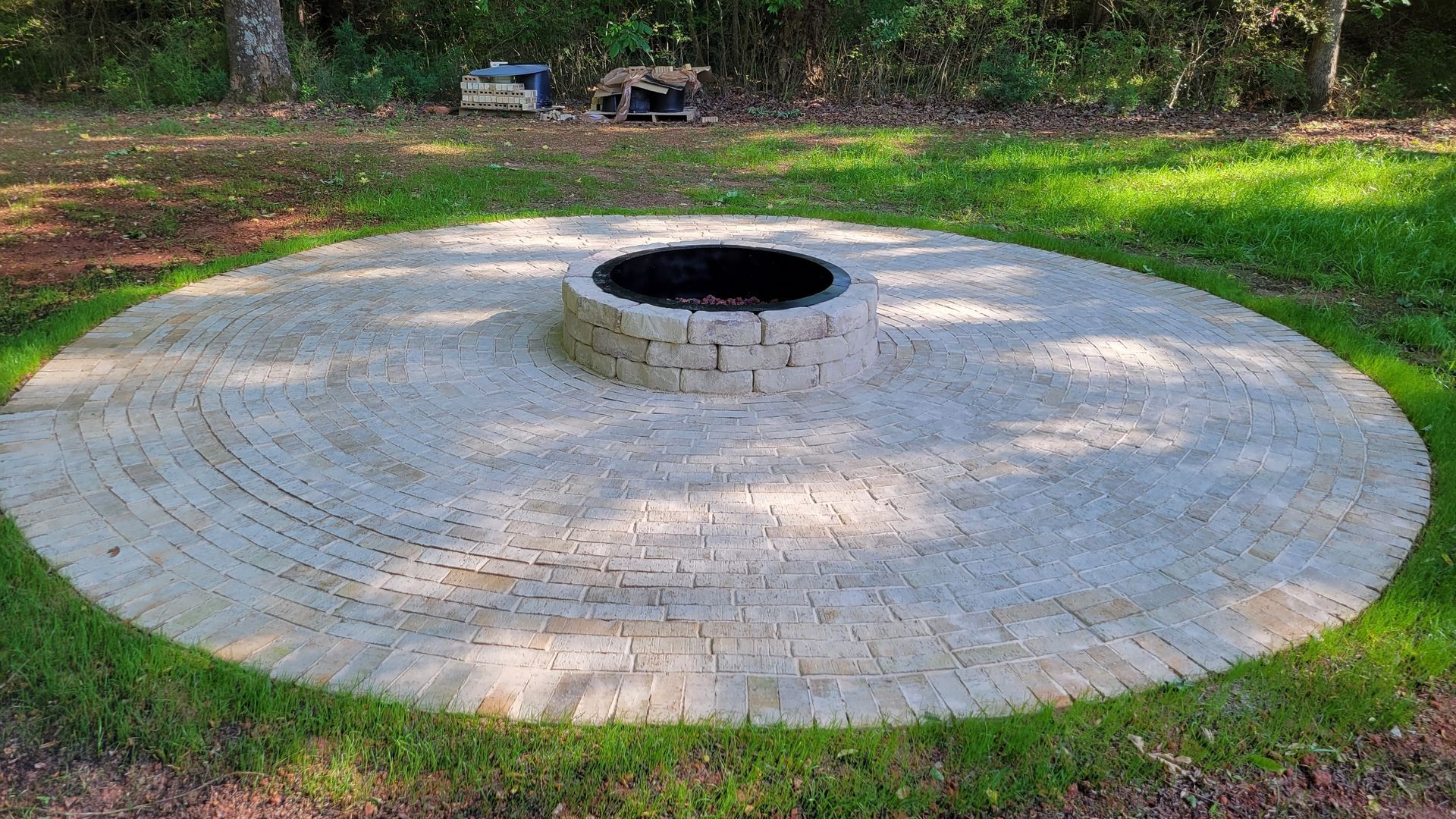 A fire pit is surrounded by bricks in the middle of a lush green field.