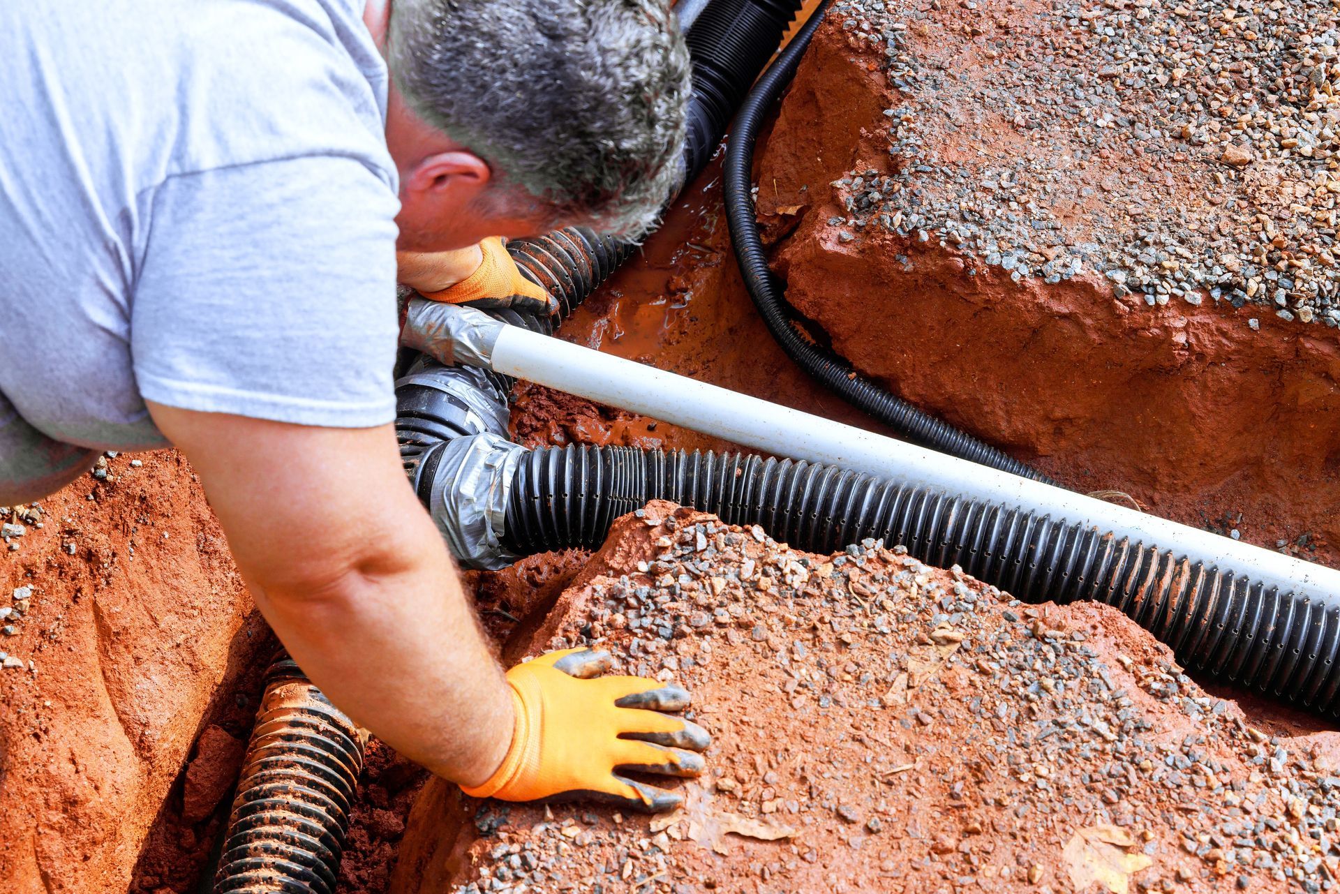 A man is using a vacuum hose to remove a pipe from the ground.