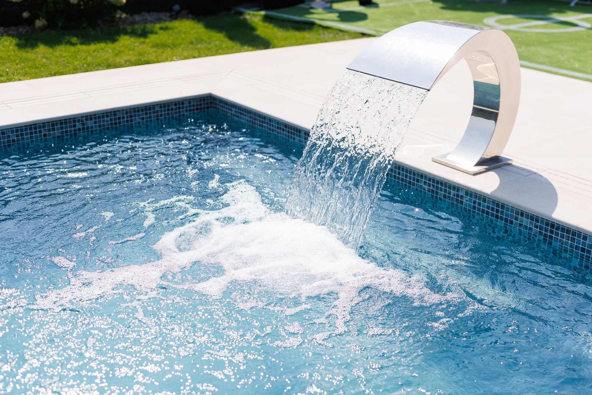A waterfall is pouring water into a swimming pool.