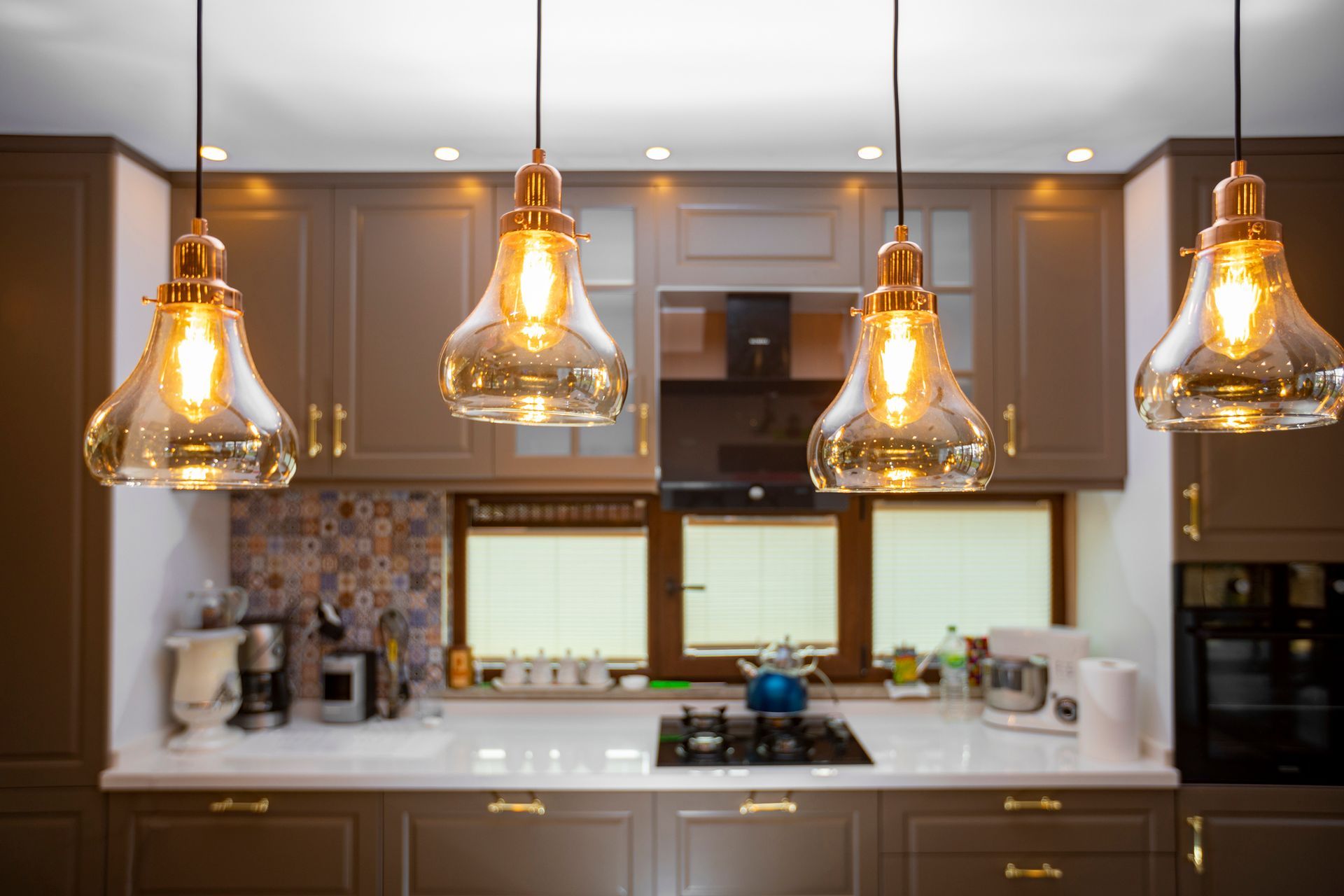 A kitchen with a stove top oven , a window , and pendant lights hanging from the ceiling.
