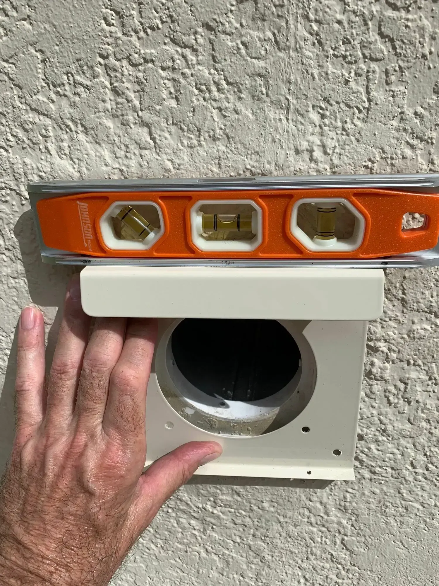Love's Dryer Vent Cleaning - A person is holding a level over a hole in a wall.