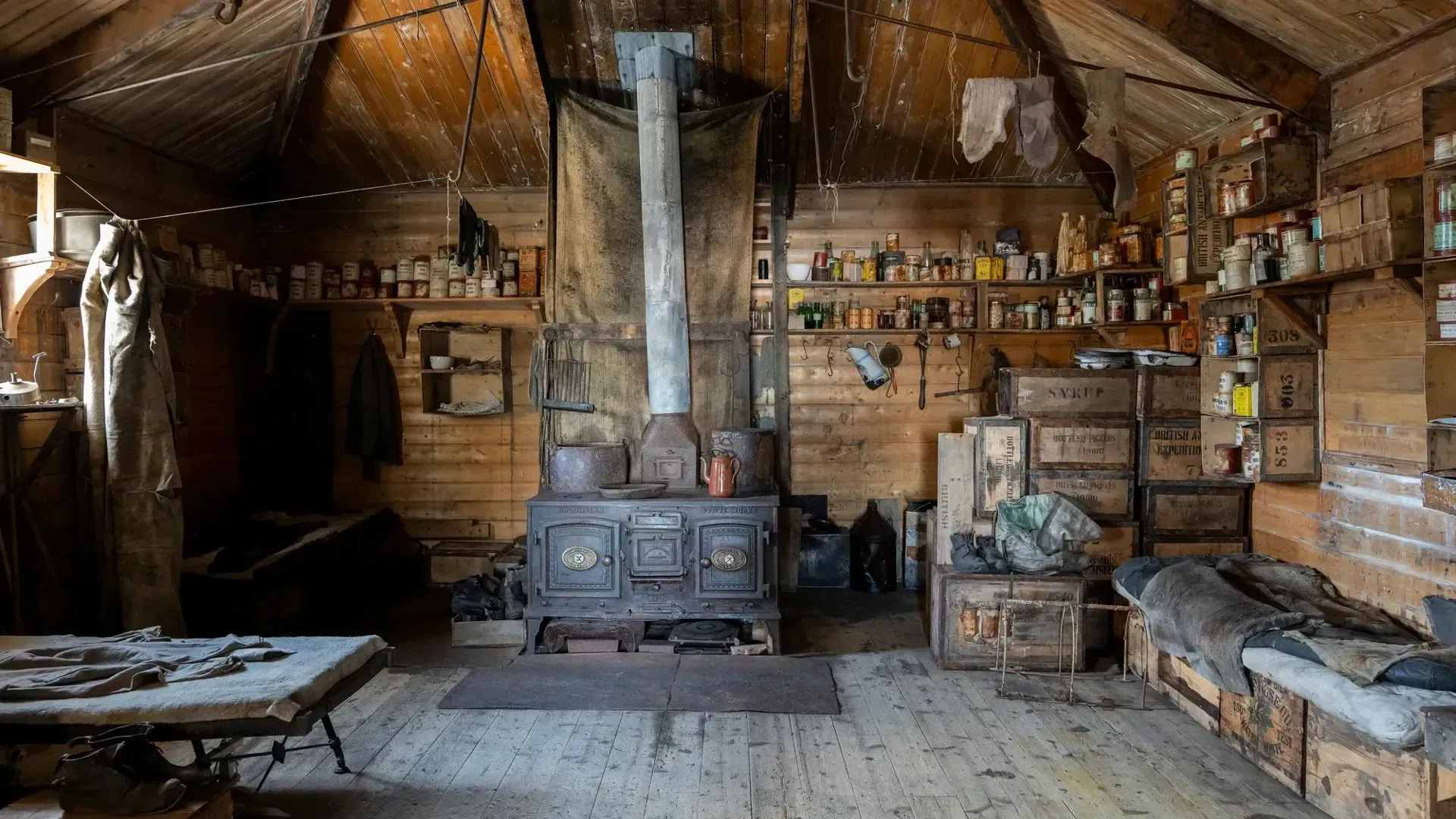 The interior of an early Antarctic explorer's hut, with wood stove, preserved supplies, and other survival gear.