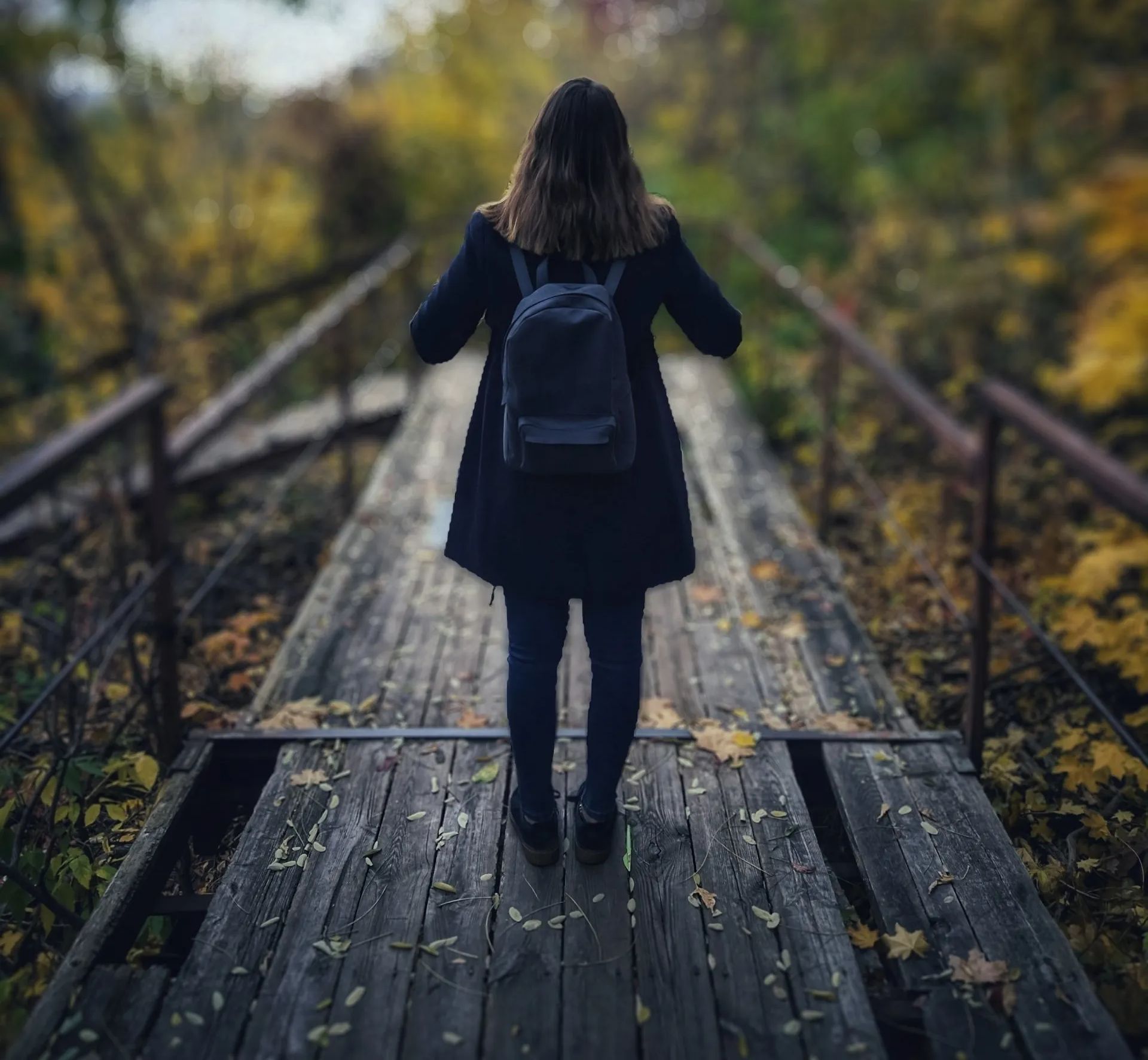 A woman with a backpack is walking across a wooden bridge