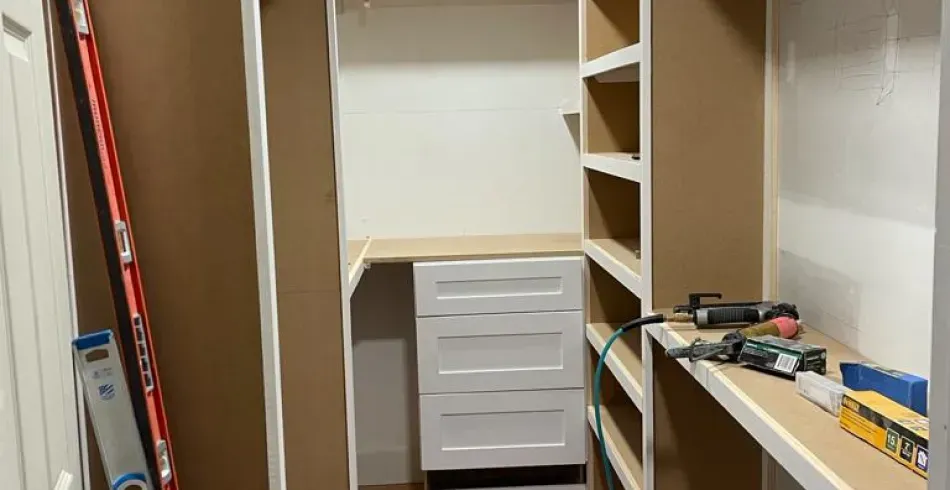 Partially built closet with shelves, a white drawer unit, and tools on the floor and counter.