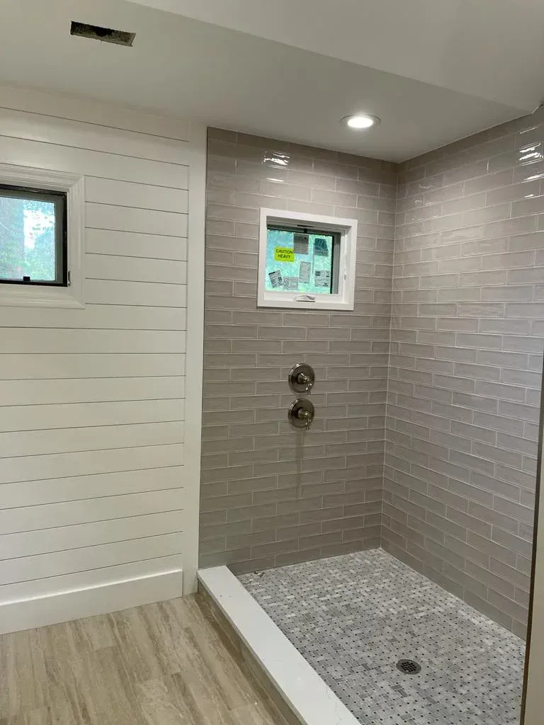 Modern shower stall with white slat wall, gray tile, pebble floor, and two small windows