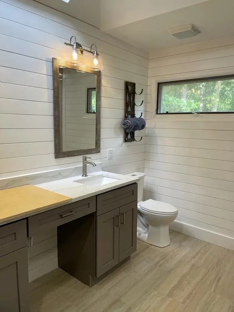 Modern bathroom with white shiplap walls, floating vanity, mirror, toilet, and window