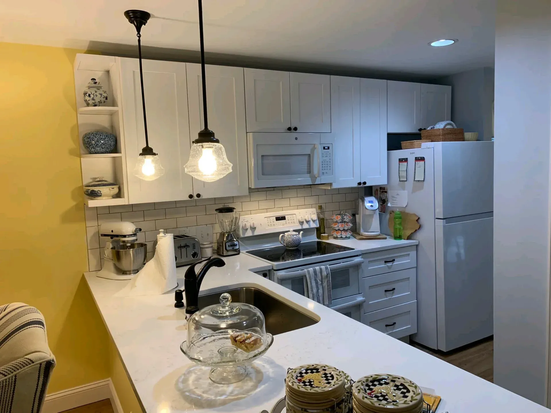 Bright white kitchen with island, pendant lights, stove, microwave, and refrigerator.